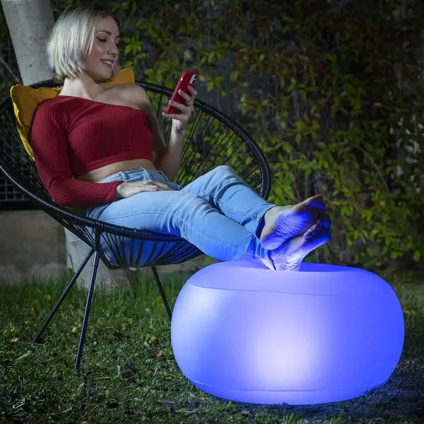 Woman relaxing on an armchair with the Pulight multicolor LED inflatable pouf.