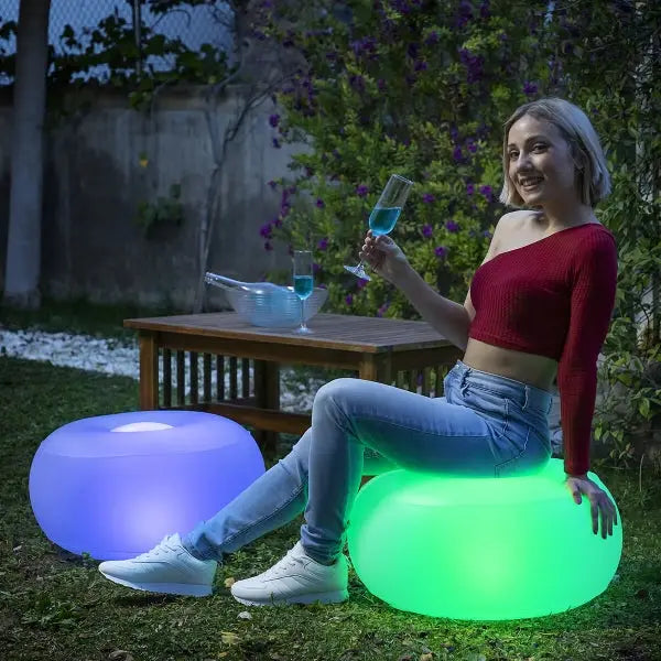 Mujer en un puf inflable LED Pulight multicolor sosteniendo una bebida.