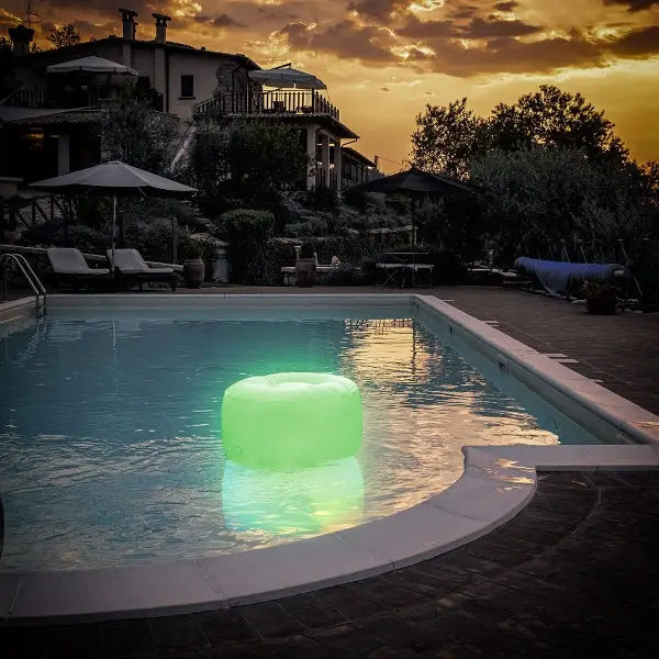 Puf hinchable Pulight con LED multicolor que brilla en la piscina al anochecer.