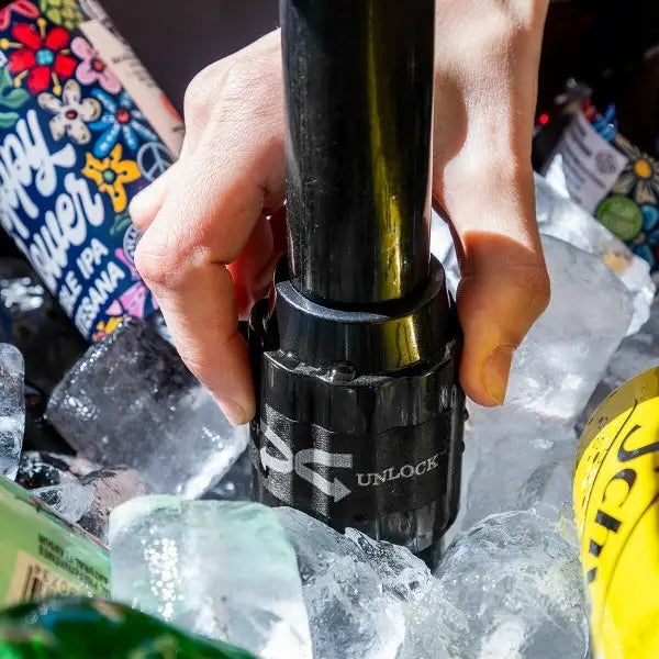 Manos sosteniendo un dispositivo cilíndrico negro con la etiqueta Desbloquear en un refrigerador de mesa.